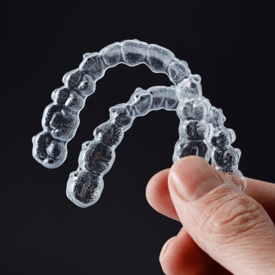 Retention: Securing Your Orthodontic Success 6 Hand holding up two retainers on black background, representing retention