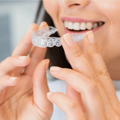 Woman inserting Invisalign clear aligners over her teeth, representing the advantages of Invisalign®